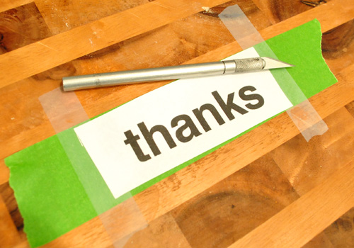 Cutting a homemade stencil of the word THANKS on a cutting board with knife