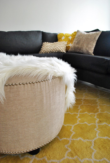 large round upholstered ottoman with nail head trim atop yellow pottery barn rug