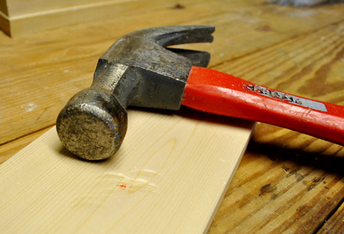 hitting hammer against new whitewood board to make it look old, distressed, and reclaimed