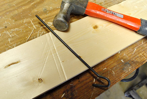 using metal rod and hammer to create long dents in new wood board to make it look old and beat up