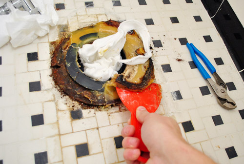 Scraping away old toilet wax ring with putty knife