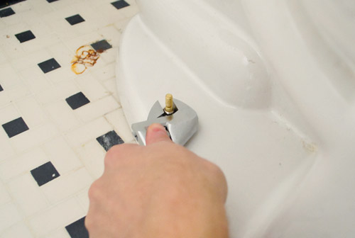 Tightening nut on toilet bowl bolts to fix rocking toilet