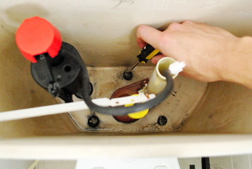 Reinstalling toilet tank by tightening screws within toilet tank
