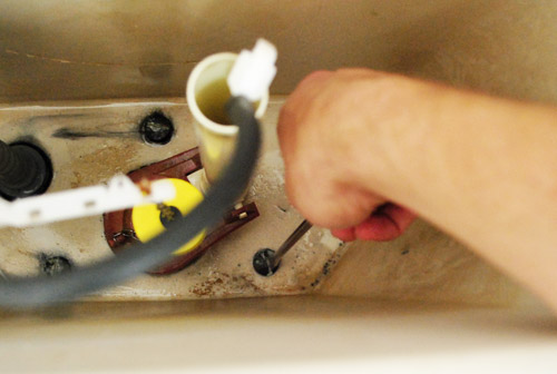 Unscrewing toilet tank from the bowl from inside the drained tank