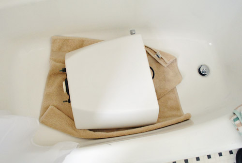 Toilet tank resting safely on soft towel in tub during repair