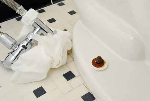 Rusty screw on base of toilet bowl causing toilet to rock