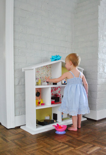 Menina brincando com casa de bonecas feita pelos pais