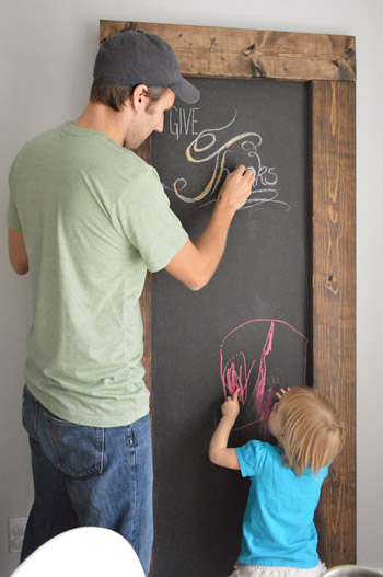 John and daughter both writing on large leaning DIY chalkboard with wood frame
