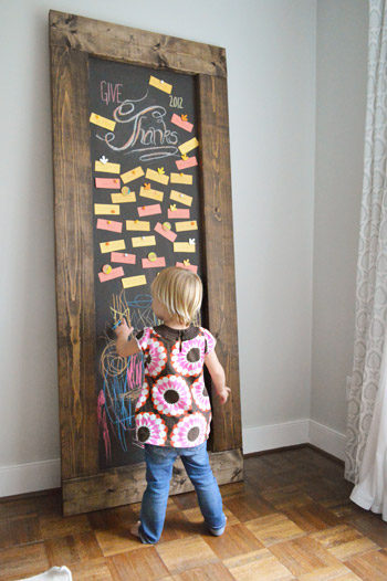 Toddler girl drawing on DIY leaning chalkboard with Thanksgiving gratitude notes