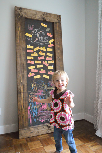 Toddler girl standing in front of DIY leaning chalkboard with Thanksgiving gratitude notes