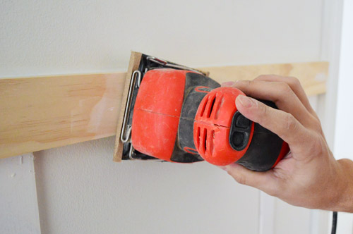 Usando a lixadeira de palma Black & Decker para alisar massa de madeira e spackle na instalação de moldagem DIY