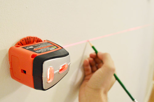 usando um nível a laser black & decker e um lápis para marcar uma linha de nível em uma parede