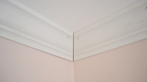 Corner of crown molding installed against ceiling with small seam at corner to be caulked