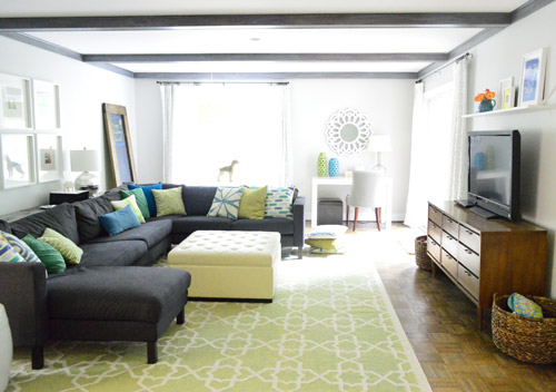 After Photo Of Living Room With Gray Beams And Large Blue Sectional On Green Rug
