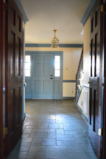 before photo of 1980s entryway foyer with williamsburg blue trim, dark wood molding, wallpaper, and discolored slate tile floor