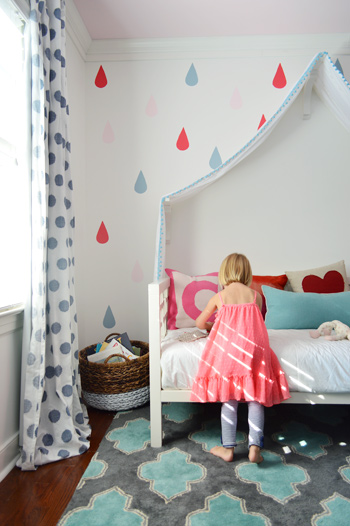 Menina brincando na cama sob o mural final de gotas de chuva sobre cama com dossel de tecido