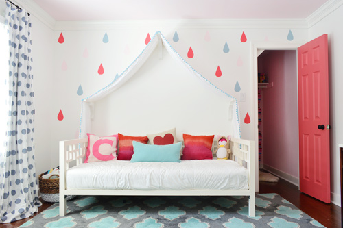 Quarto de menina com mural colorido de gotas de chuva ao redor da cama de dia com dossel e porta do armário aberta