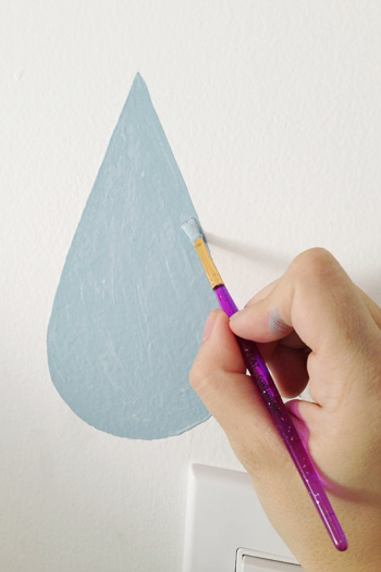 Pintura à mão de gota de chuva azul em mural de parede com pincel pequeno