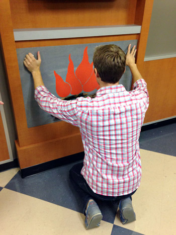 John placing fake fireplace DIY onto mantle in childrens hospital waiting room