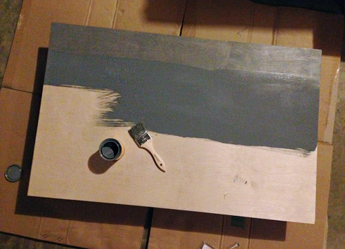 Staining a piece of plywood gray with a brush to make a faux fireplace mantle