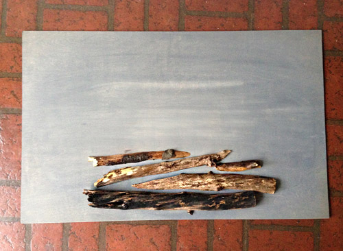 Cut tree branches stacked on gray stained plywood sheet for DIY holiday faux fireplace