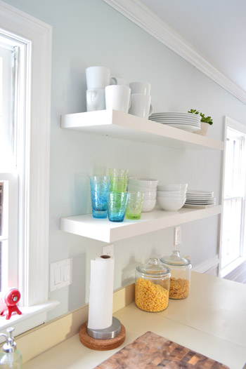 two long Ikea floating shelves in a kitchen holding colorful cups and stacks of white dishware