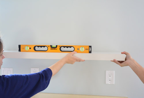 using a level to mark placement of Ikea floating shelves on kitchen wall