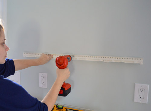 attaching metal hanging bracket for Ikea floating shelf using a drill driver to screw it to kitchen wall 