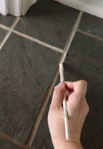 applying Oyster Gray PolyBlend Grout Renew to dirty tile grout lines with paintbrush