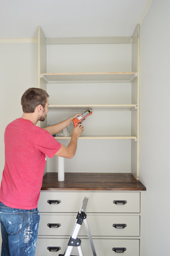 Man caulking under shelf of built in bookshelf