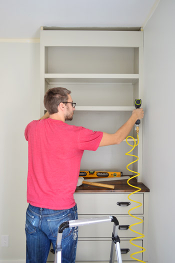 Man nailing trim pieces on the face of DIY bookshelf