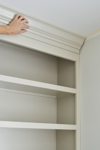 Hand holding crown molding piece in place on DIY bookshelf