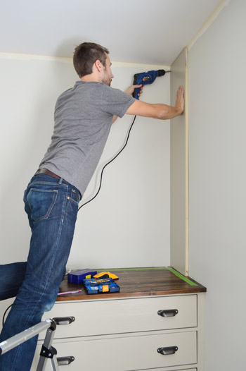 Man attaching side piece of bookshelf attached to a wall