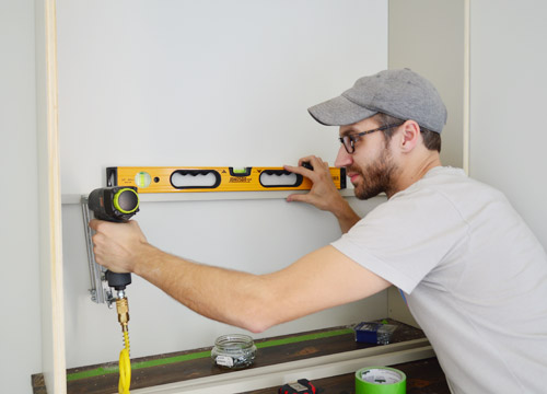 Man using level to nail in shelf support pieces