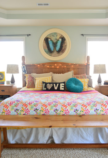 Large Bed With Funky Pillows And String Lights On Headboard
