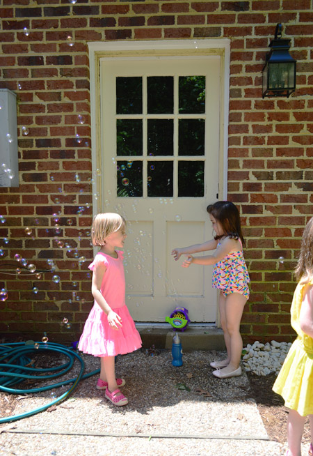 Girls Playing With Bubbles At Kids Birthday Party In Front Of Brick Wall And Unpainted Garage Door