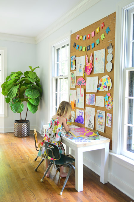 child working on art below giant cork board wall with drawings and painting pinned up