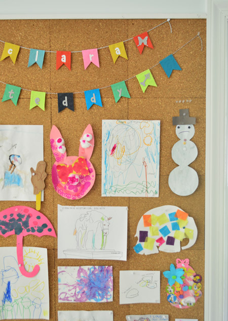 close up detail of kids art hung on cork board wall including name banner bunting from etsy