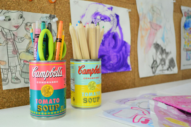 latas de sopa Campbell's de edição limitada com rótulos de Warhol usadas para guardar lápis e giz de cera na mesa de artes das crianças