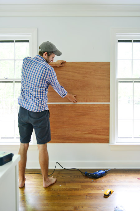 dry fitting plywood planks on wall between two windows to become base for gluing cork board tiles to create cork board wall