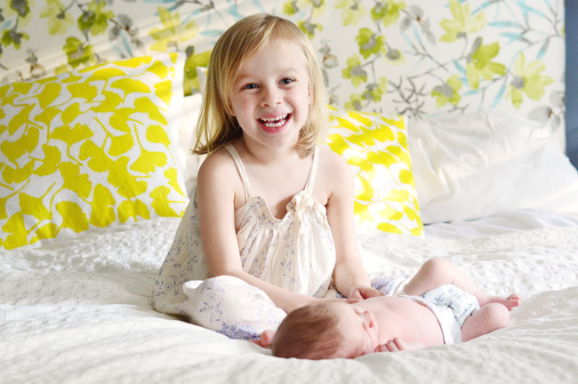 Big Sister Photo With Newborn Baby Brother In Front Of Colorful Background Fabric