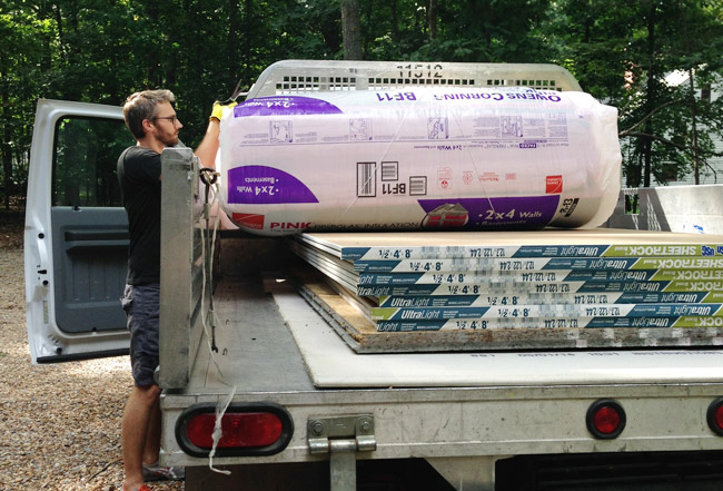 John lifting insulation out of truck bed with sheets of sheetrock in the back too