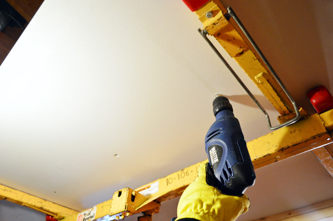 attaching drywall sheet to the ceiling using a drill