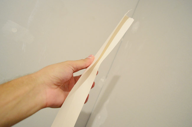 hand folding drywall tape along seam before pressing in corner 