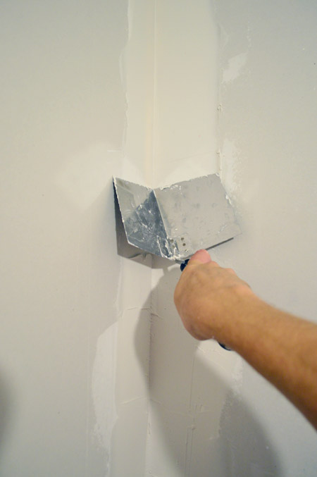 John smoothing drywall mud in corner of room using corner trowel