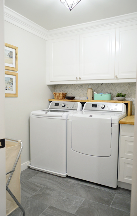 Finished laundry room with gray floor tile and marble backsplash