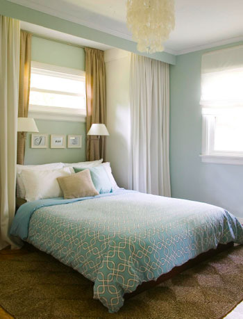 blue bedroom with curtain panels on all sides creating built in nook with wall sconces with blue bedspread and jute rug and capiz chandelier